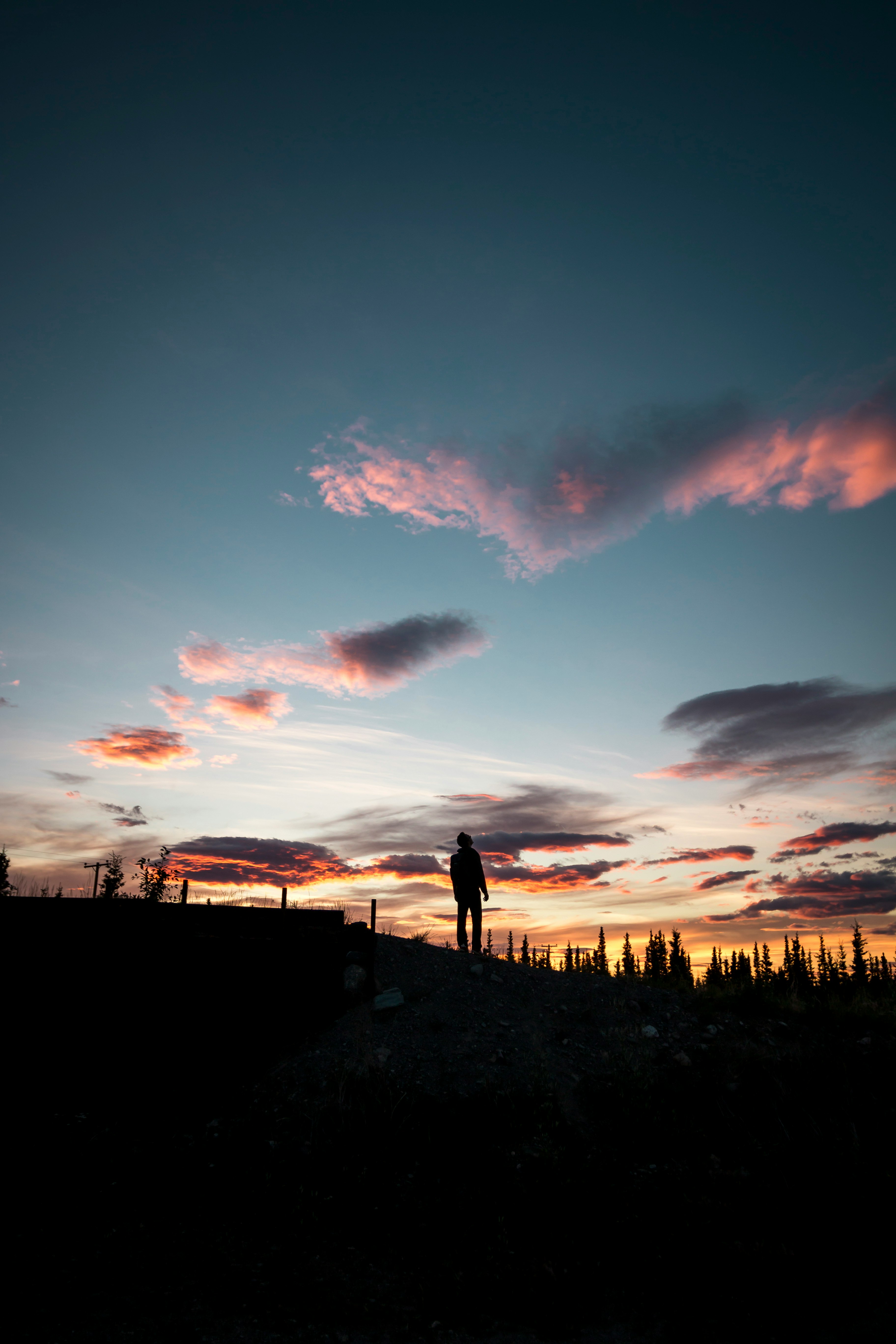 man standing on hill under gray and orange sky at golden hour